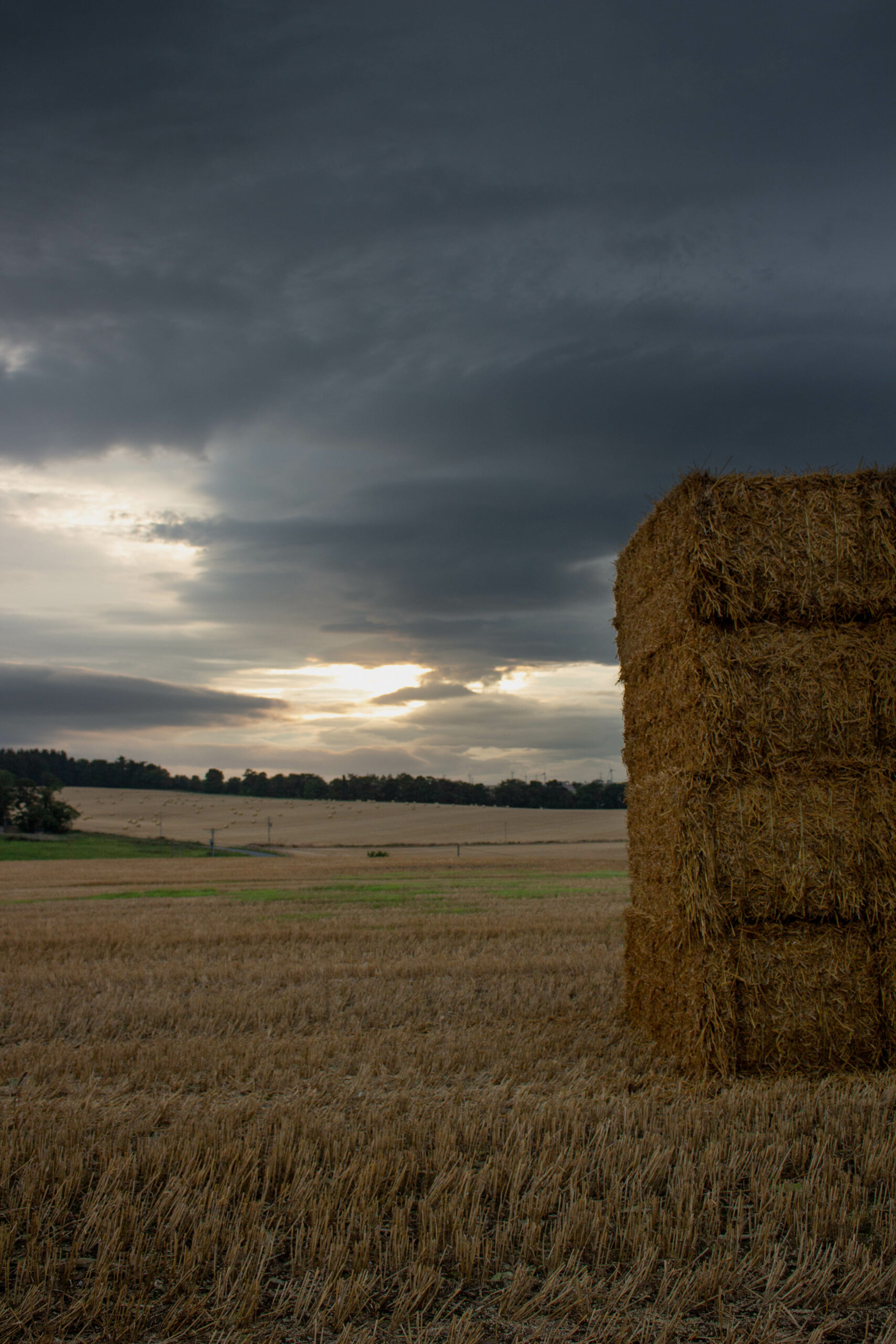 Sunset with Dark clouds over farm land and bales